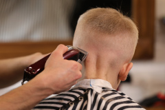 Men's hairstyling, haircutting, in a barber shop or hair salon. Close-up of man hands grooming kid boy hair in barber shop. Boy cut with hairdresser's machine.